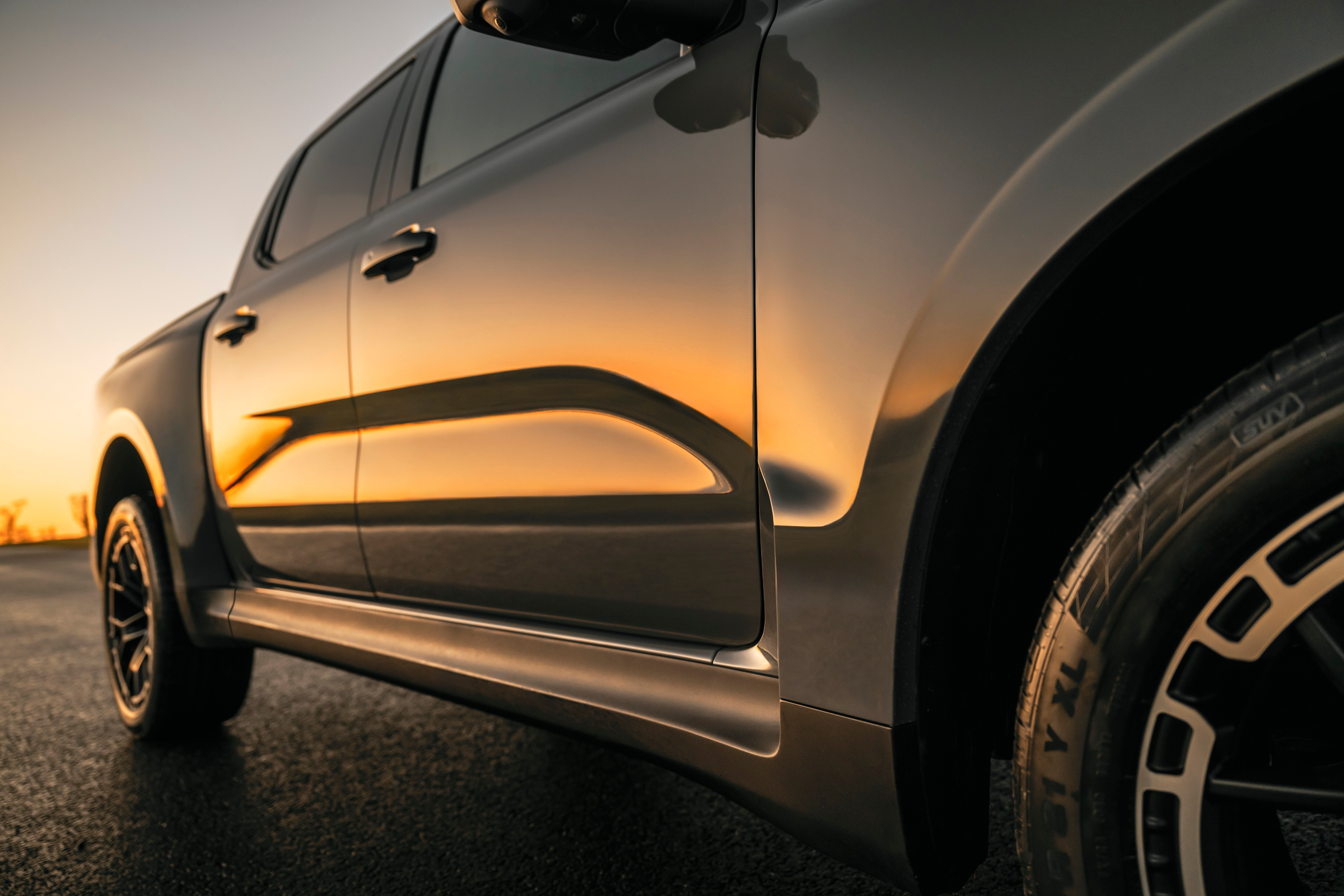 A closeup of a grey pickup reflecting a sunset