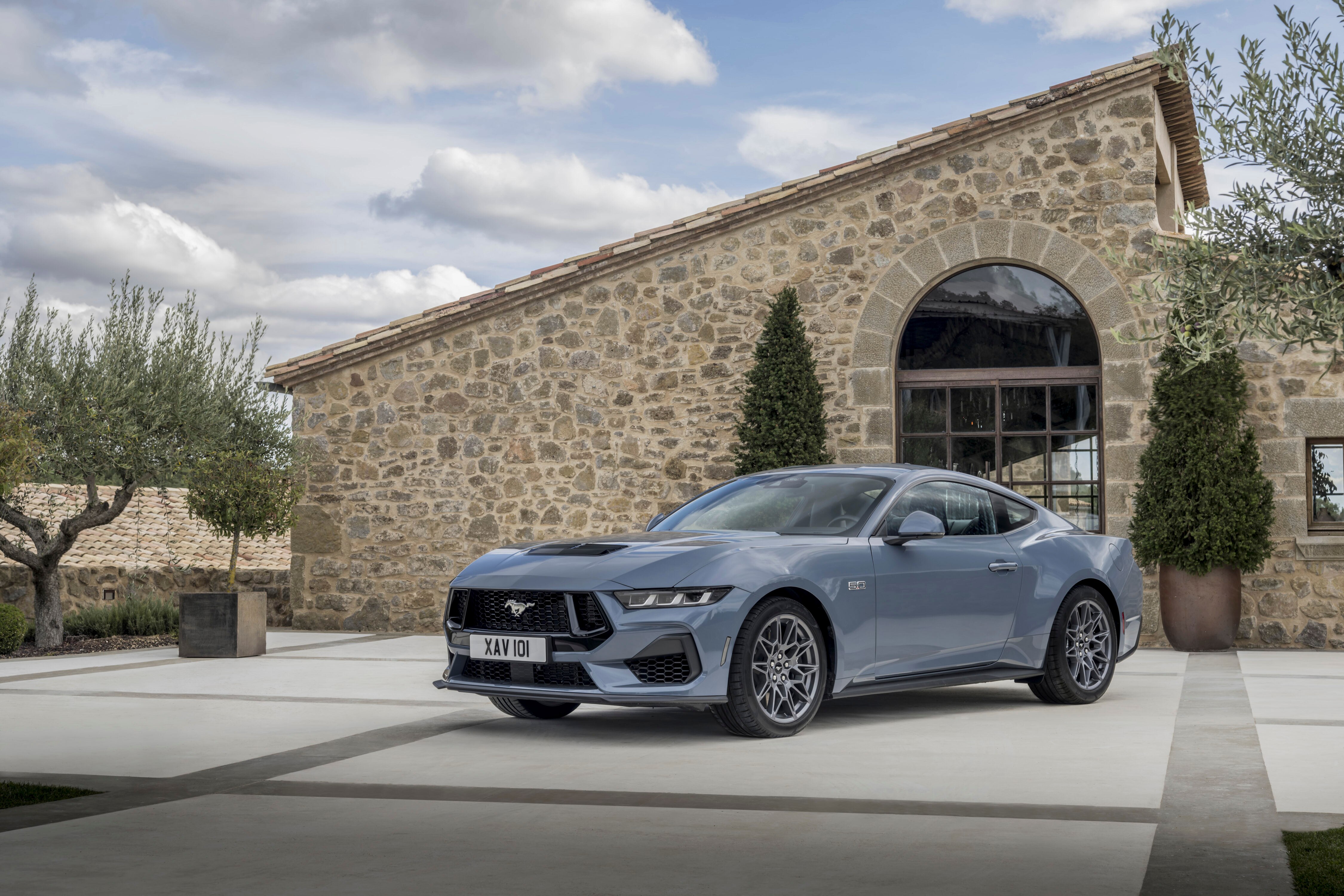 a blue Ford Mustang parked outside a rustic house