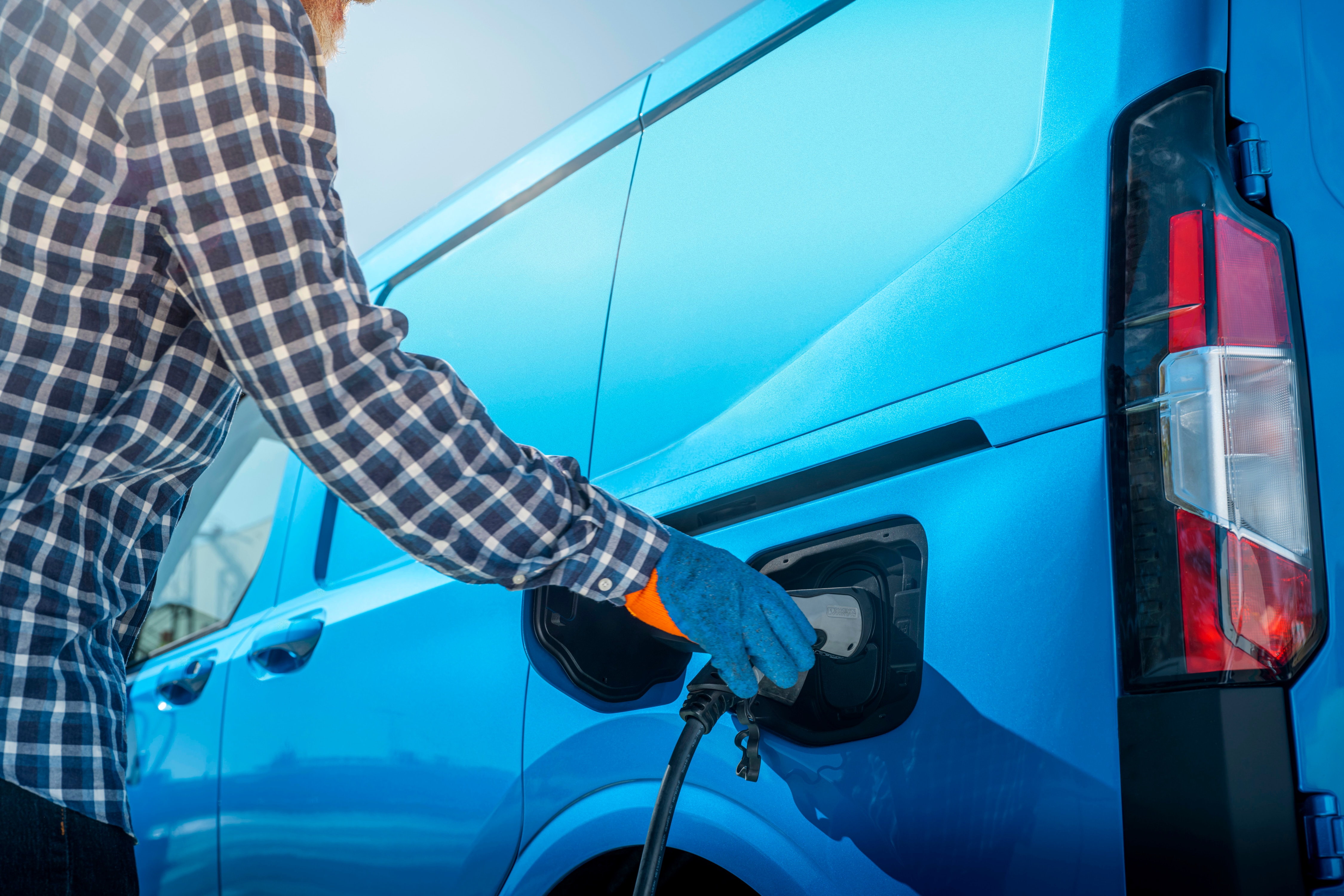 Driver plugging a blue Ford Pro electric van into charger