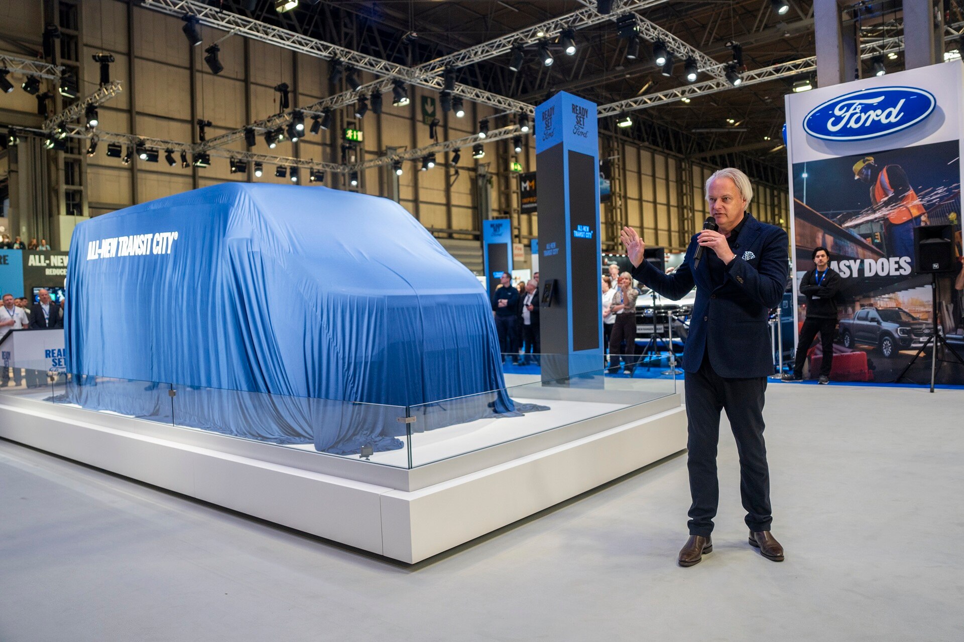 Ford Pro general manager Hans Schep making a speech next to Transit City still covered by a blue silk