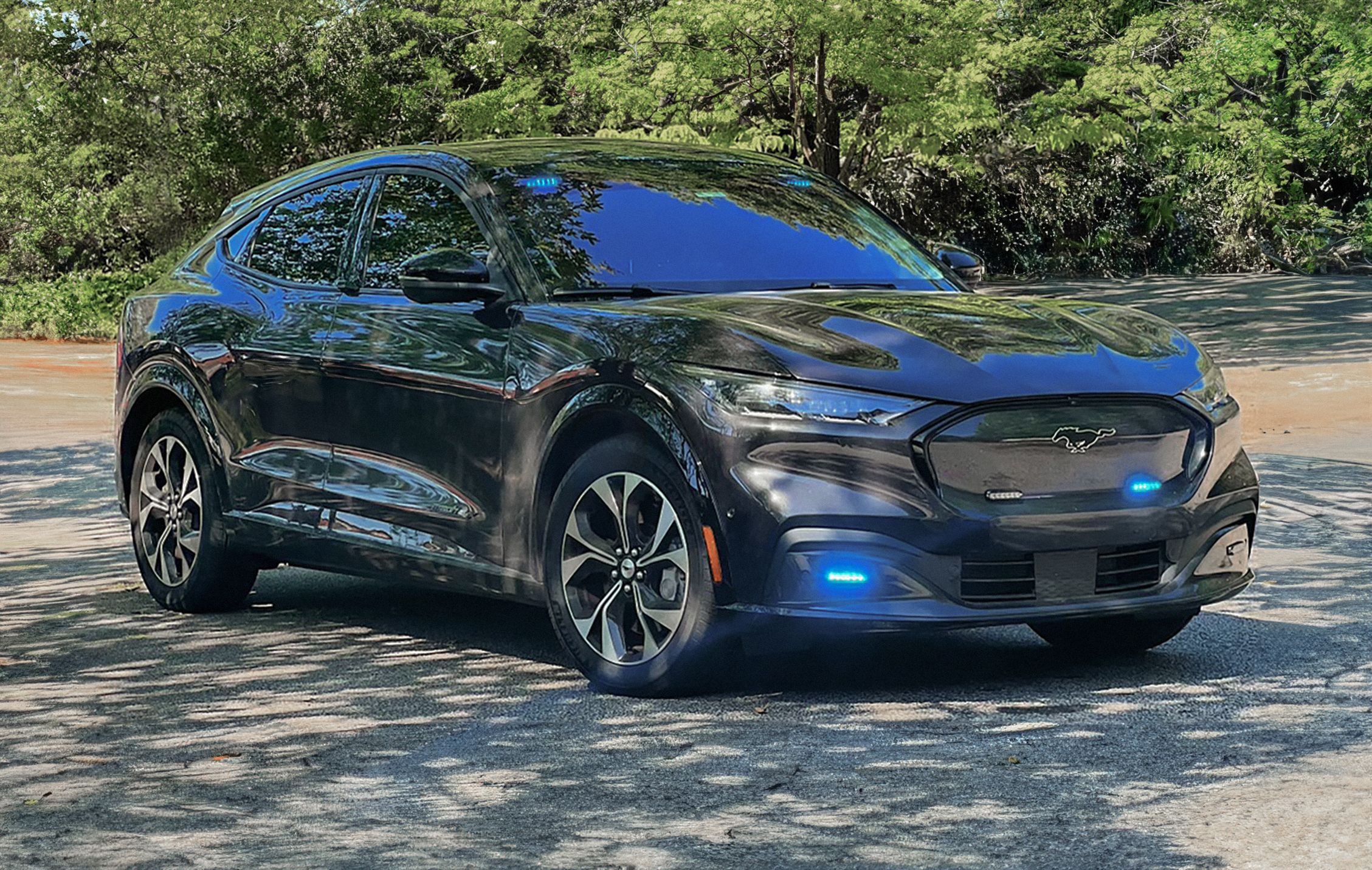 A Mustang® Mach-E® SUV with its lights on parked in the shade