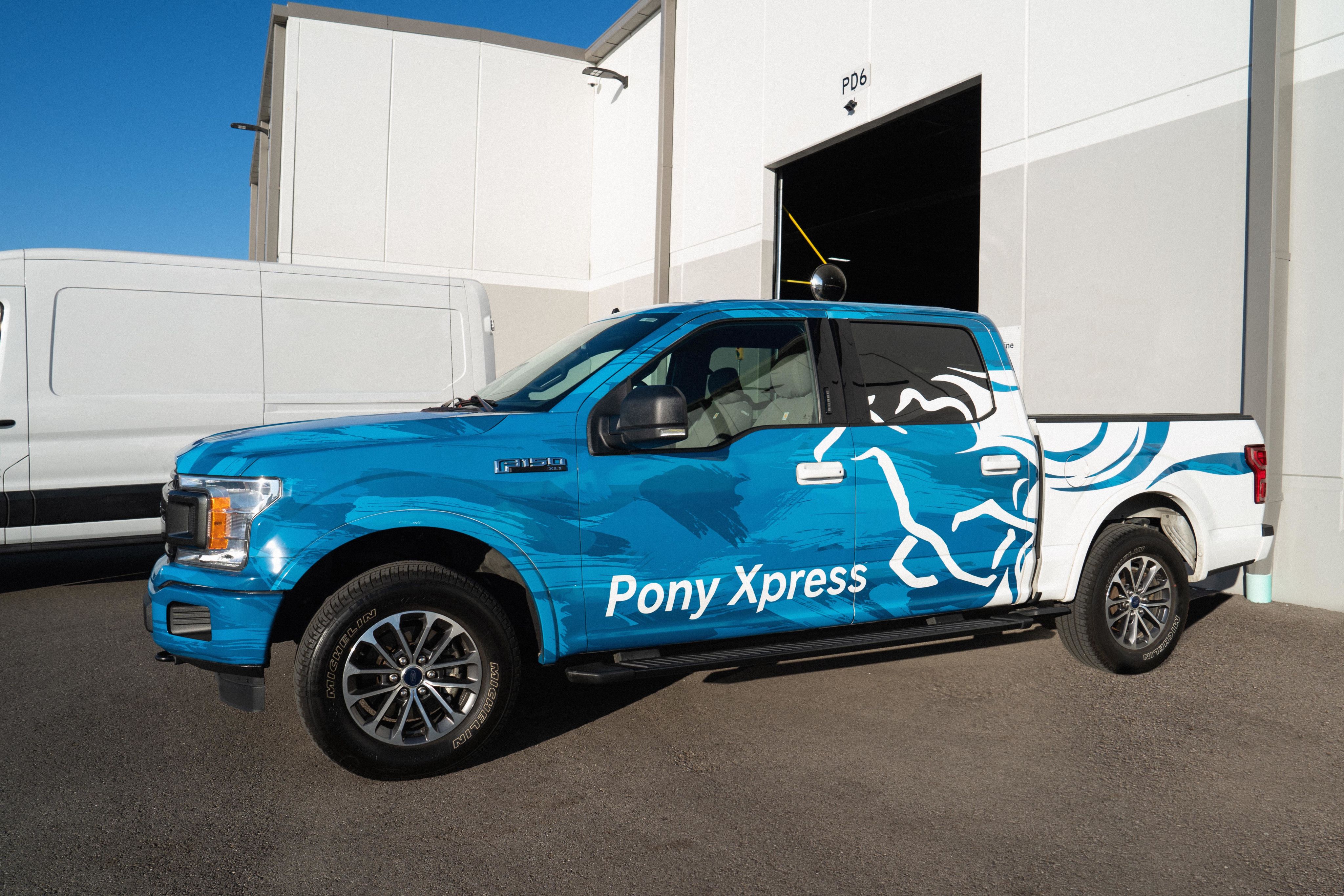 An F-150 XLT with a Pony Xpress custom wrap parked in front of the warehouse.