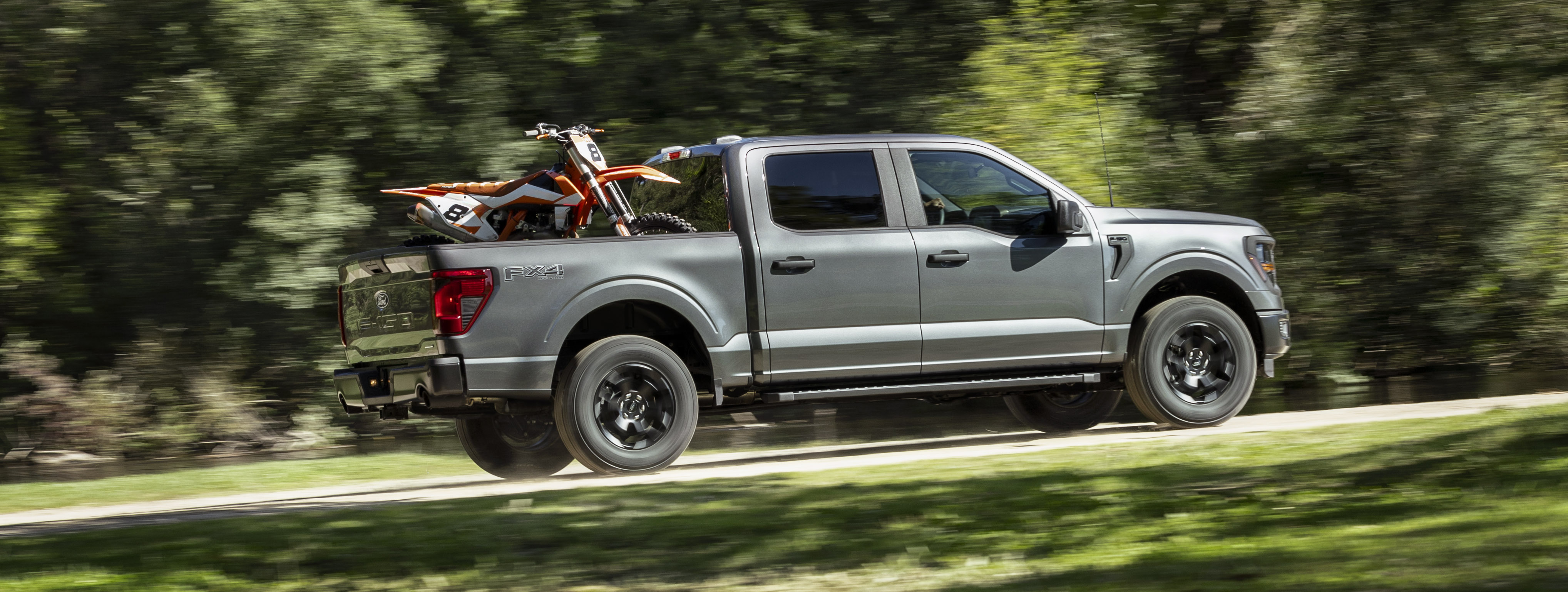 A 2024 Ford F-150 STX tows a motor bike in the bed.