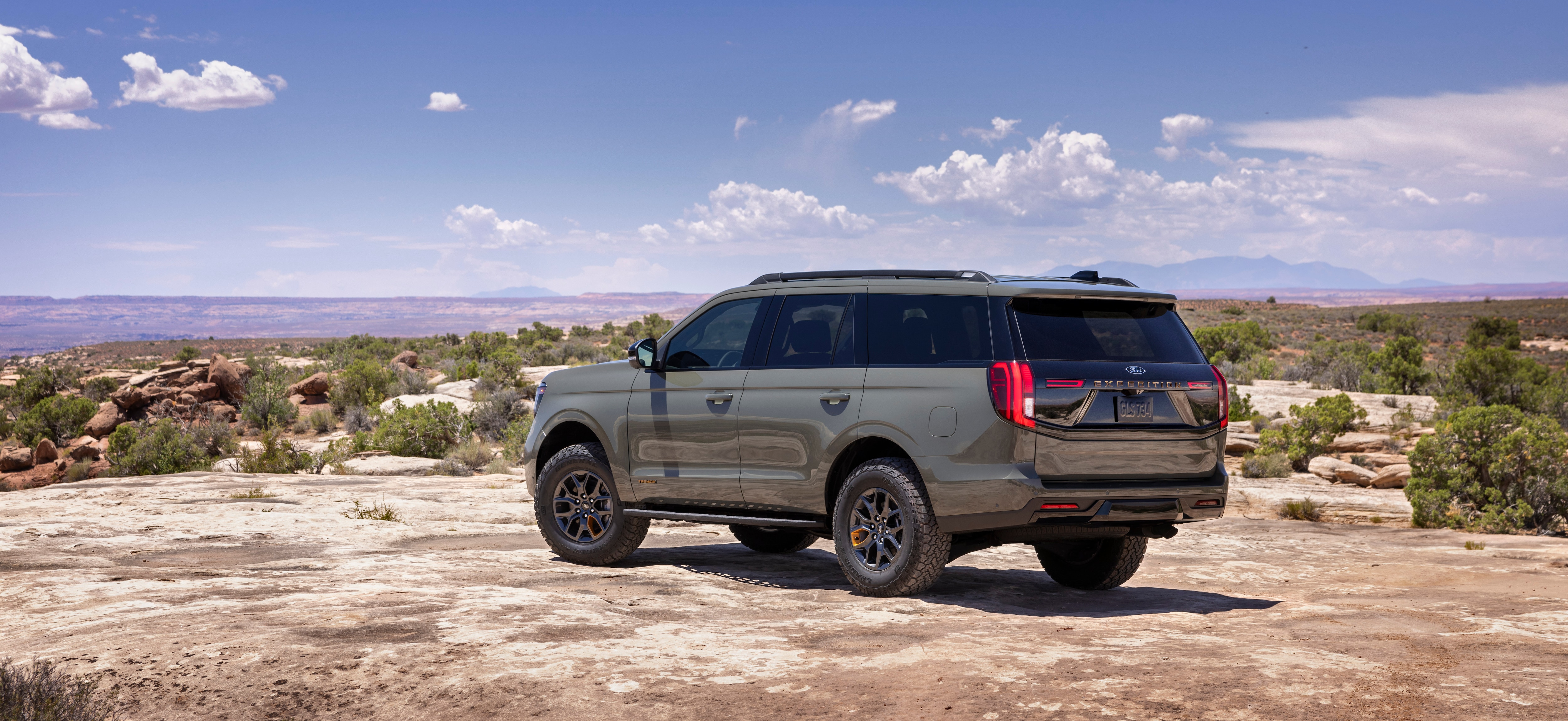 2025 Ford Expedition Tremor parked on rugged terrain, a blue sky and desert area with shrubs behind it. 