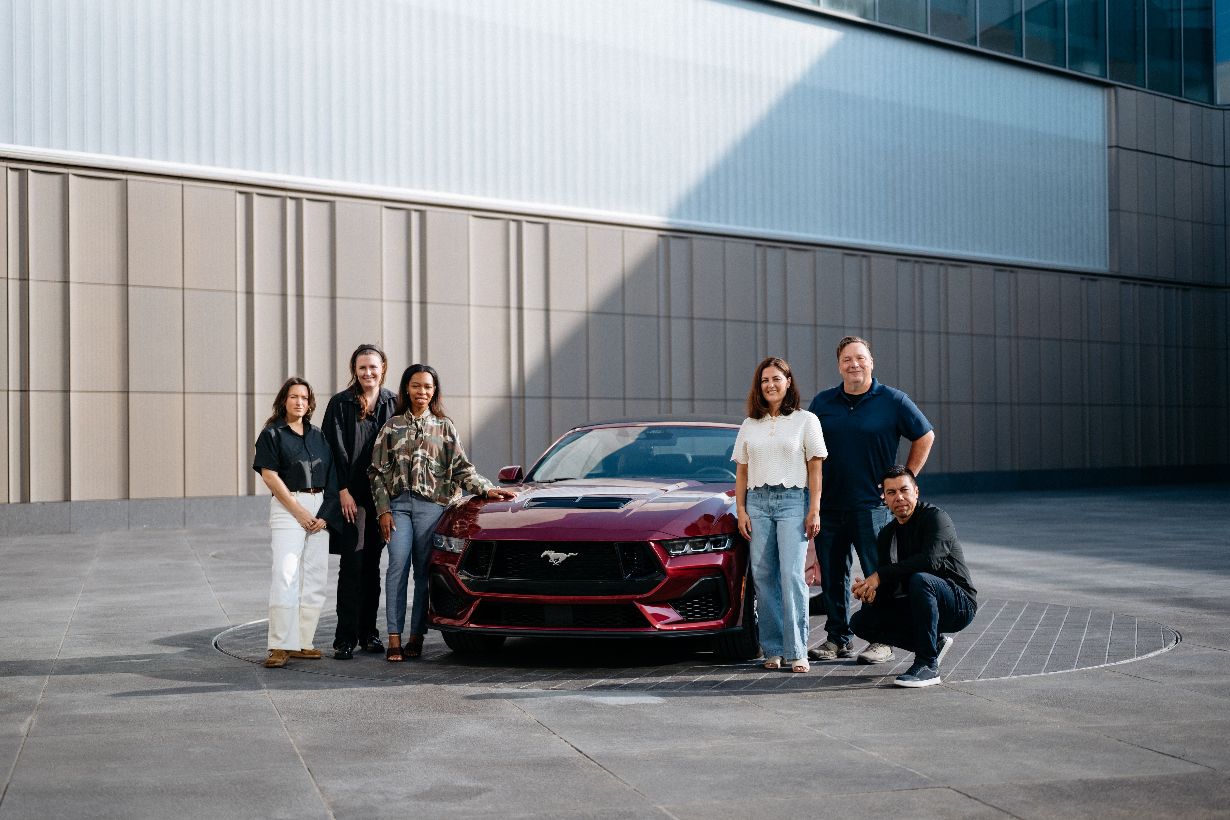 A group of 4 people pose with a Ford Mustang in the new color of Molten Magenta.  