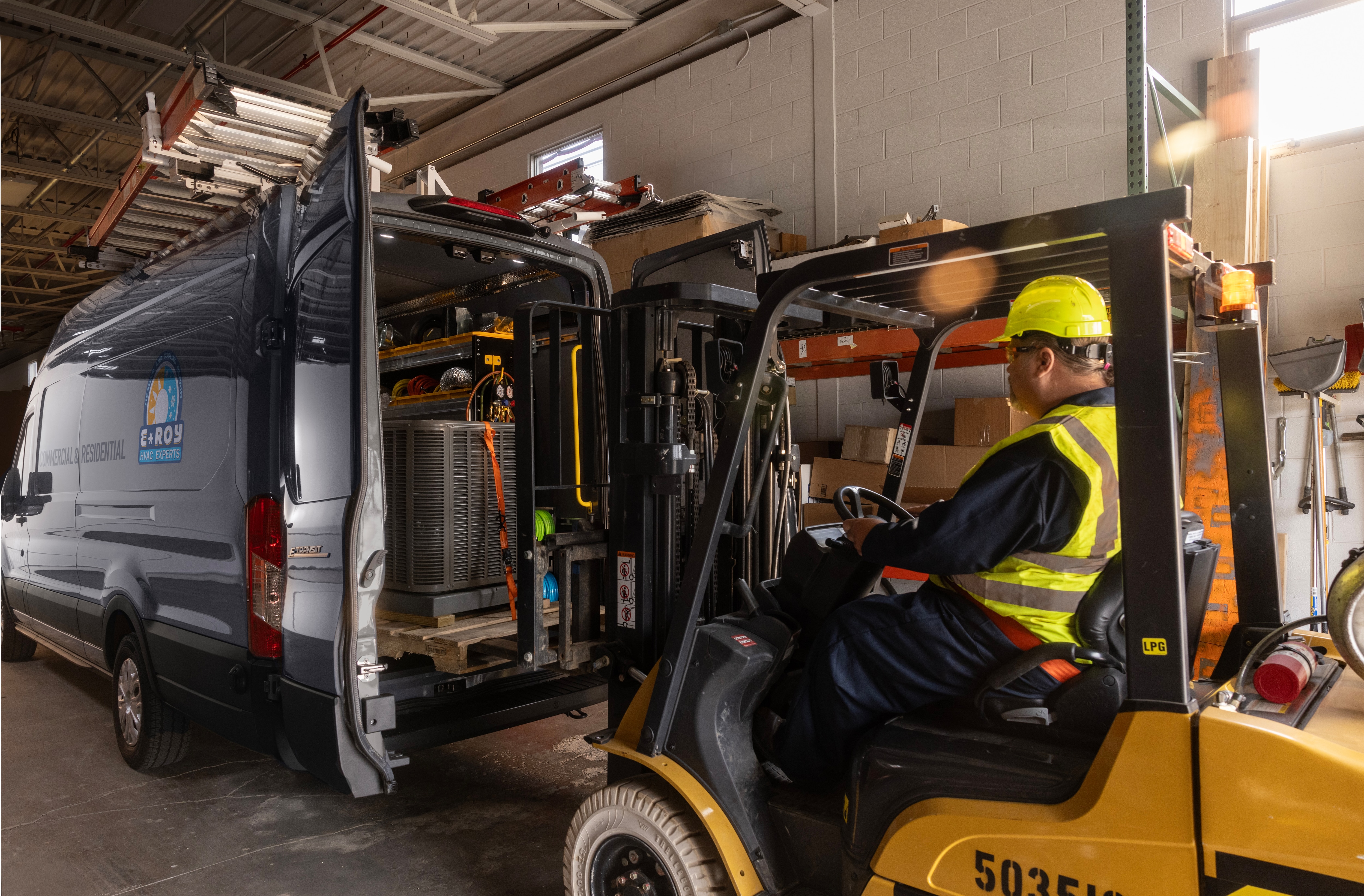 A worker loads an AC unit into the back of an E-Transit van.