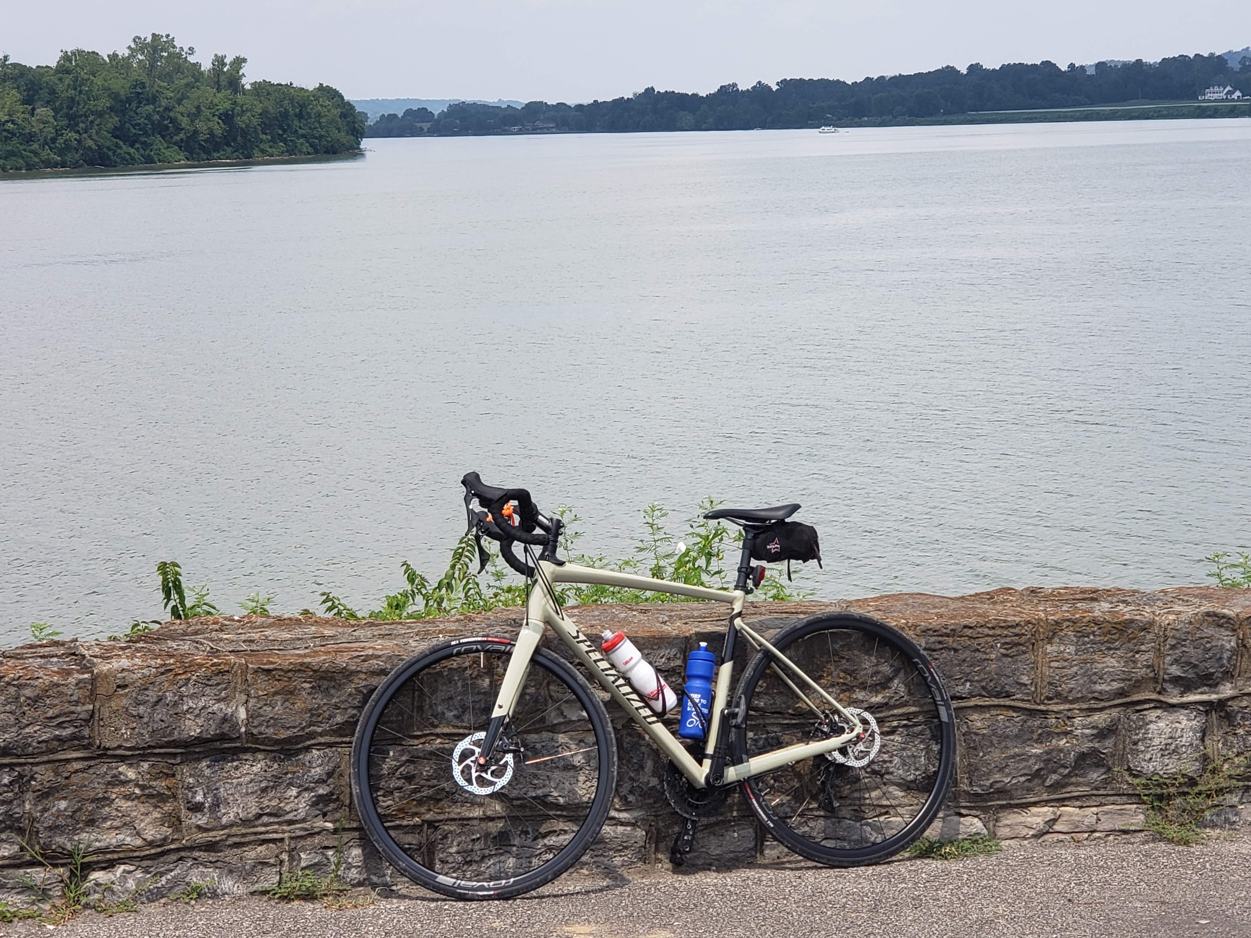 A bicycle leans against a short stone wall in front of a body of water.