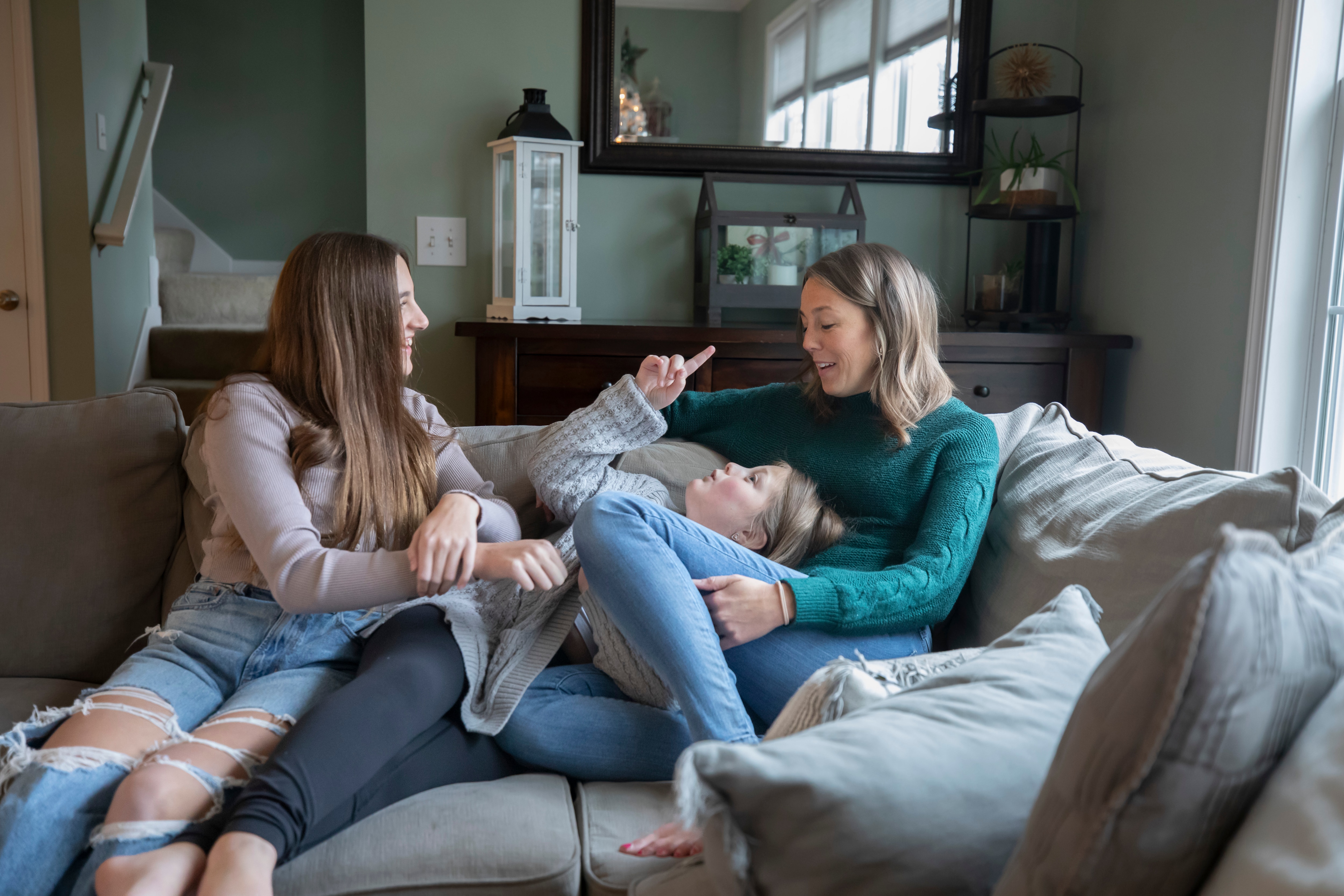 A woman sits on a couch in her living room with her two daughters.