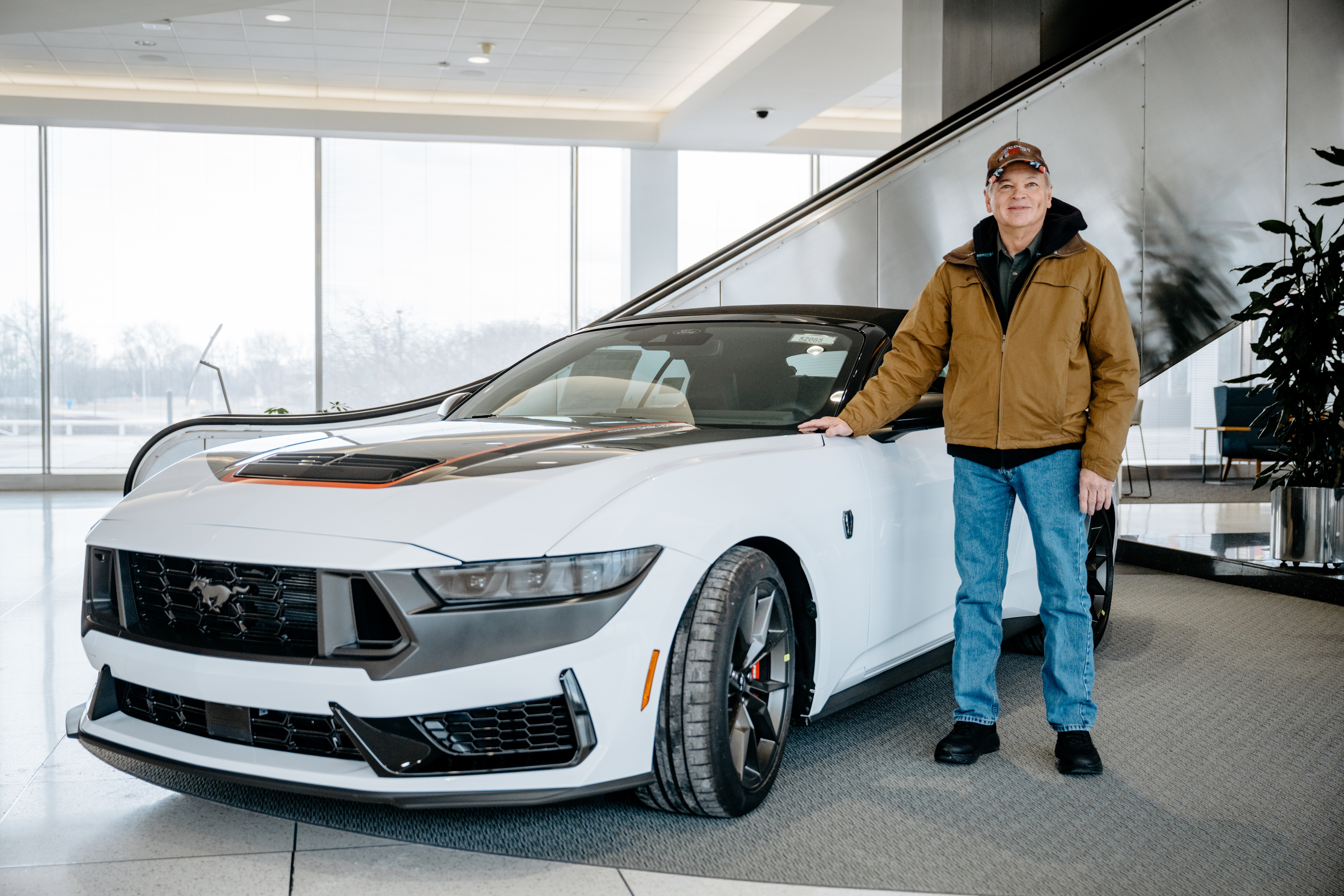 A man stands next to a brand new convertible. 