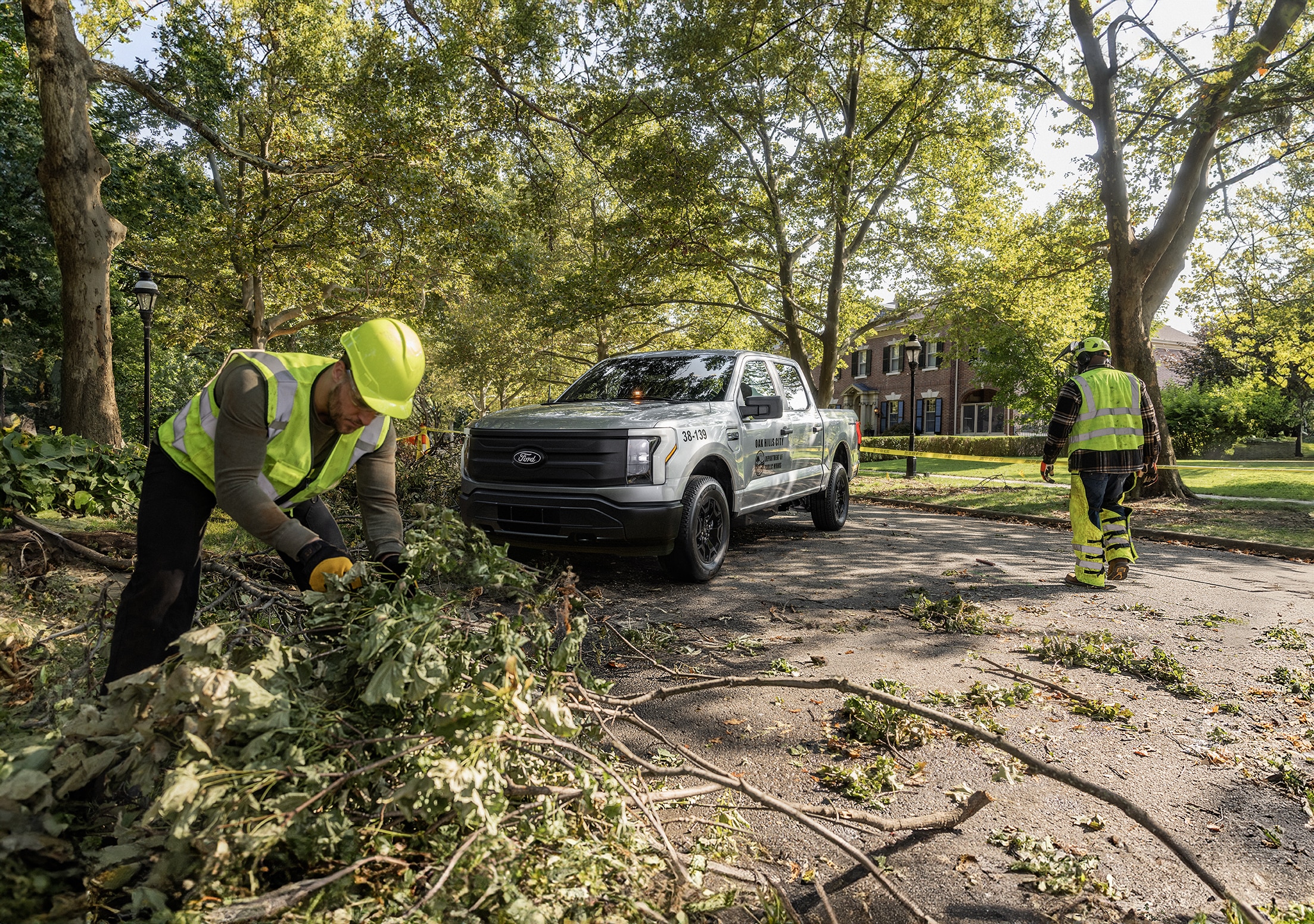 People in yellow vests pick up tree debris from a street.