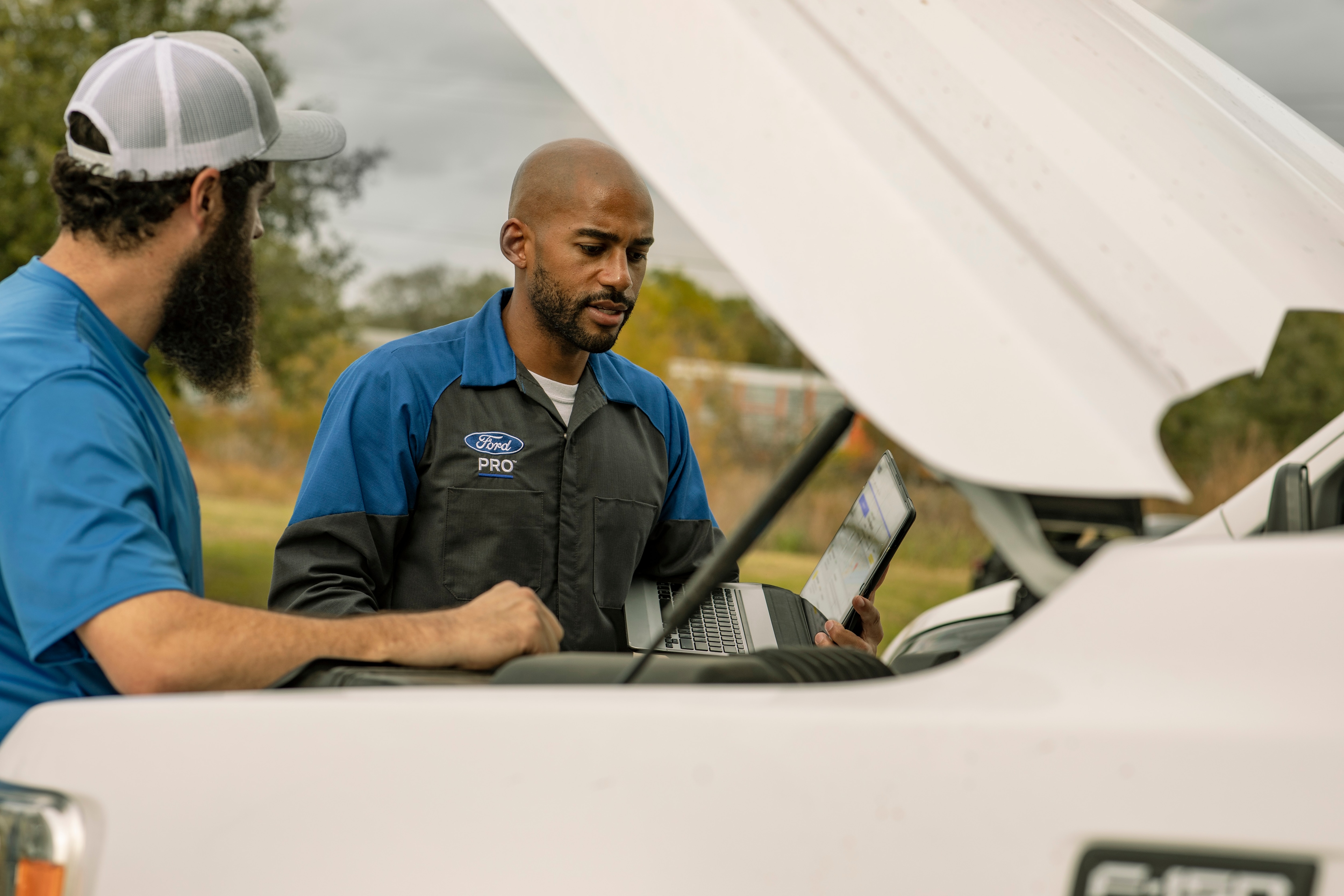 A Ford Mobile Service technician looks under the hood of a Ford truck with a customer. 