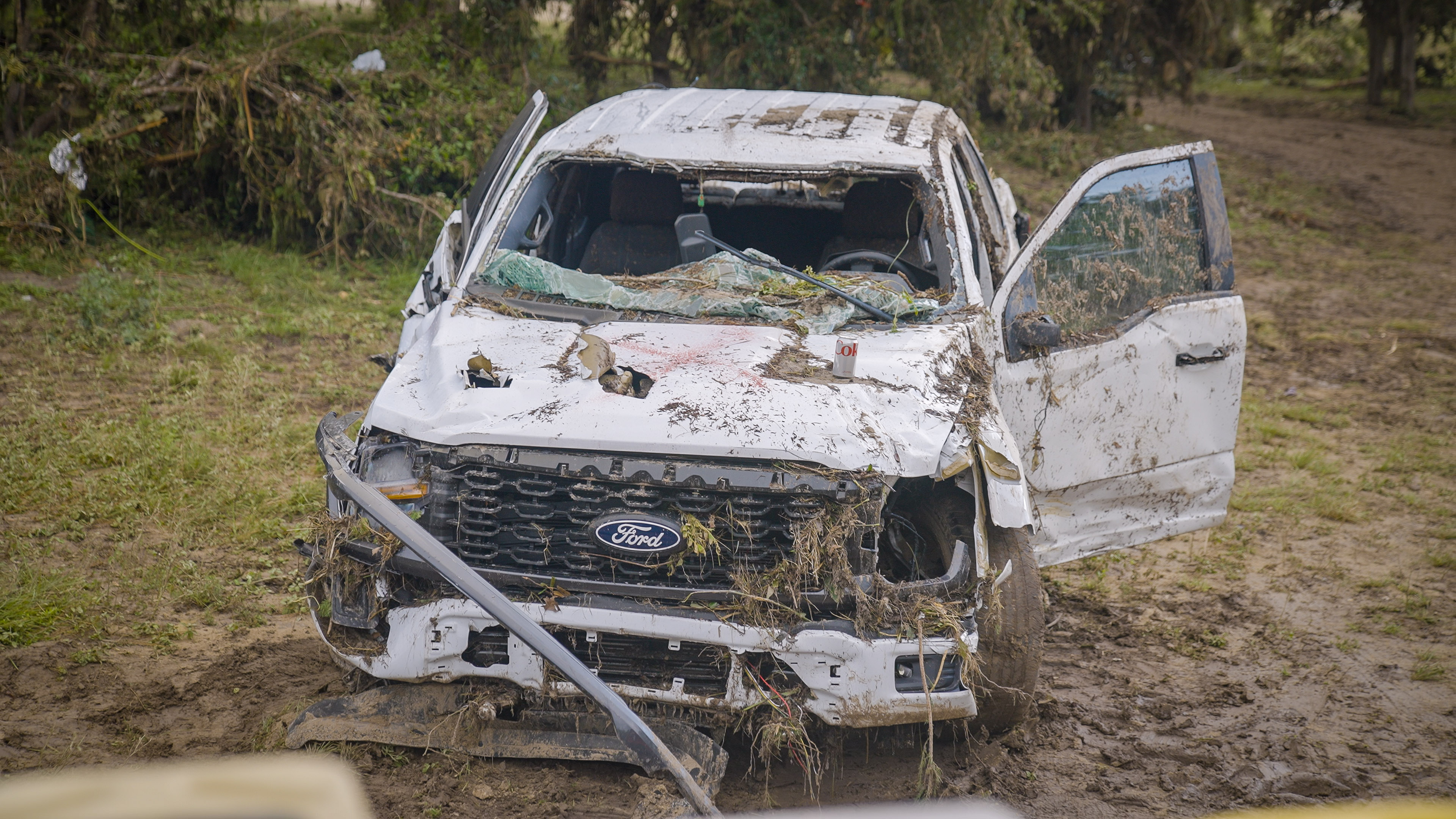 A white Ford truck covered in dirt and debri and smashed up after a flood.