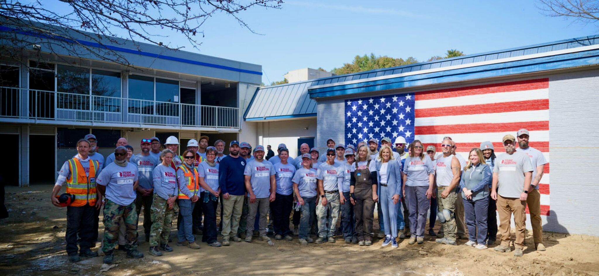 A group of volunteers poses for a photo in front of a building with an American flag on its side.