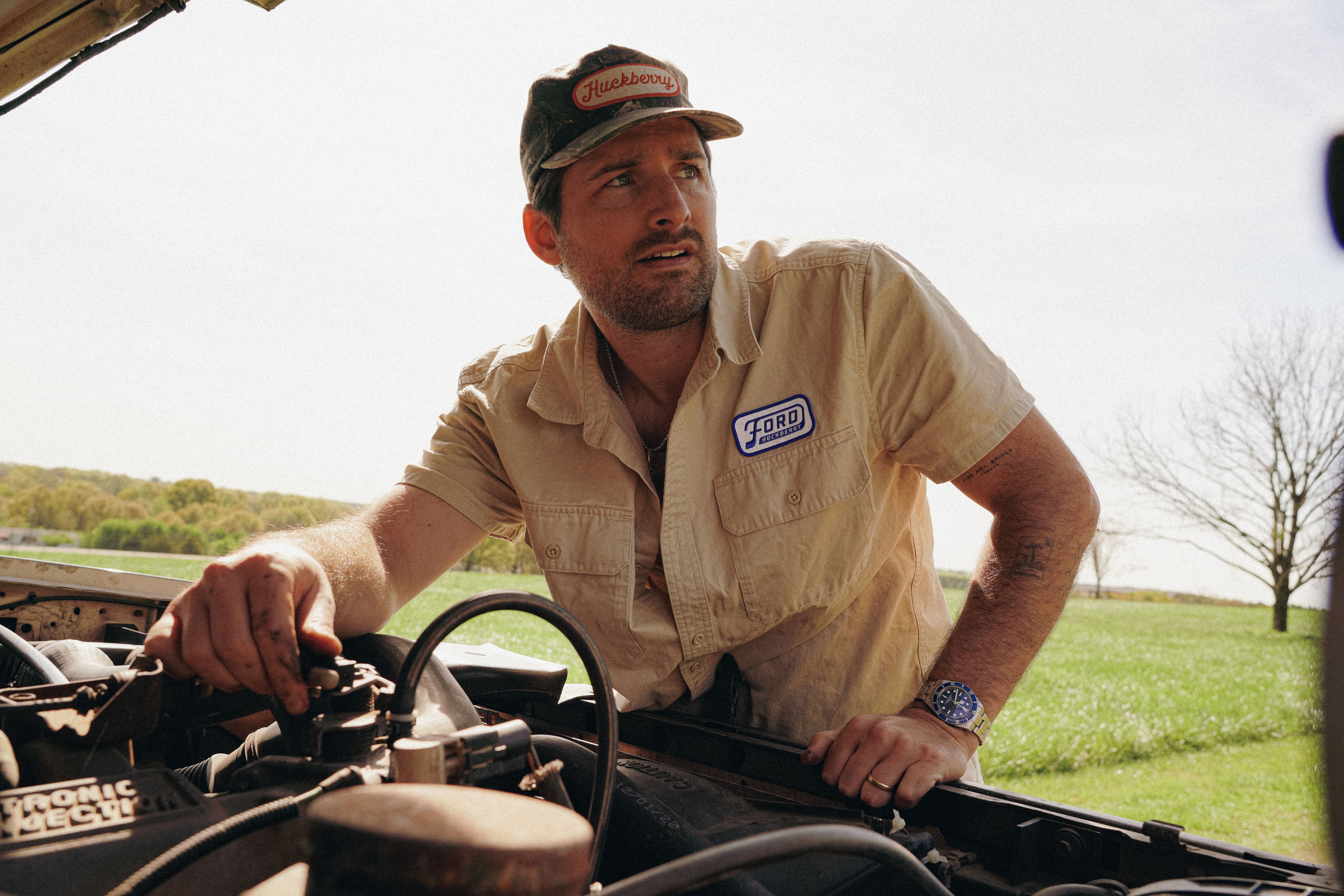 A man wearing a Huckberry x Ford shirt stands under the hood of a truck
