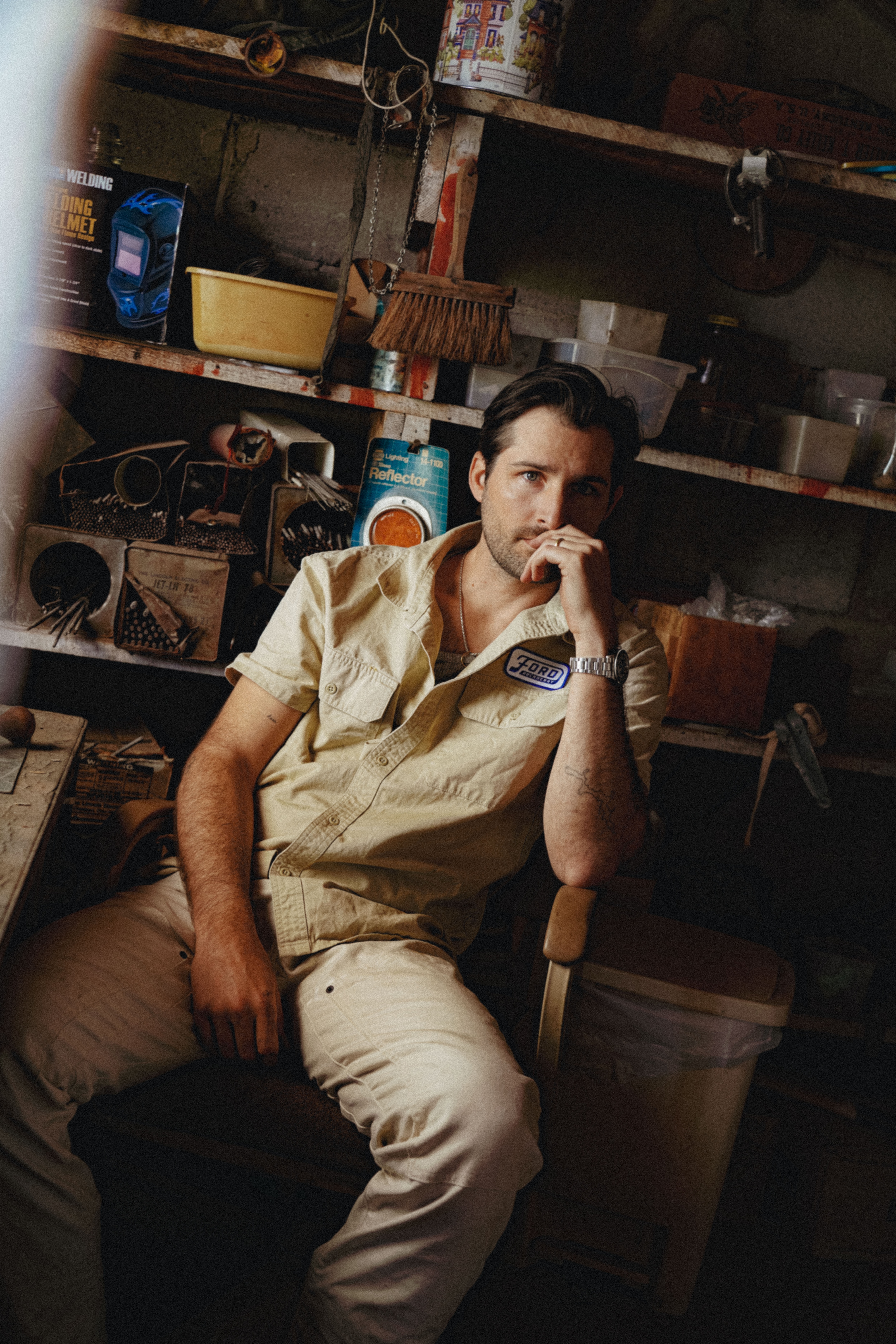 A man wearing a Huckberry x Ford shirt poses, sitting, in a garage