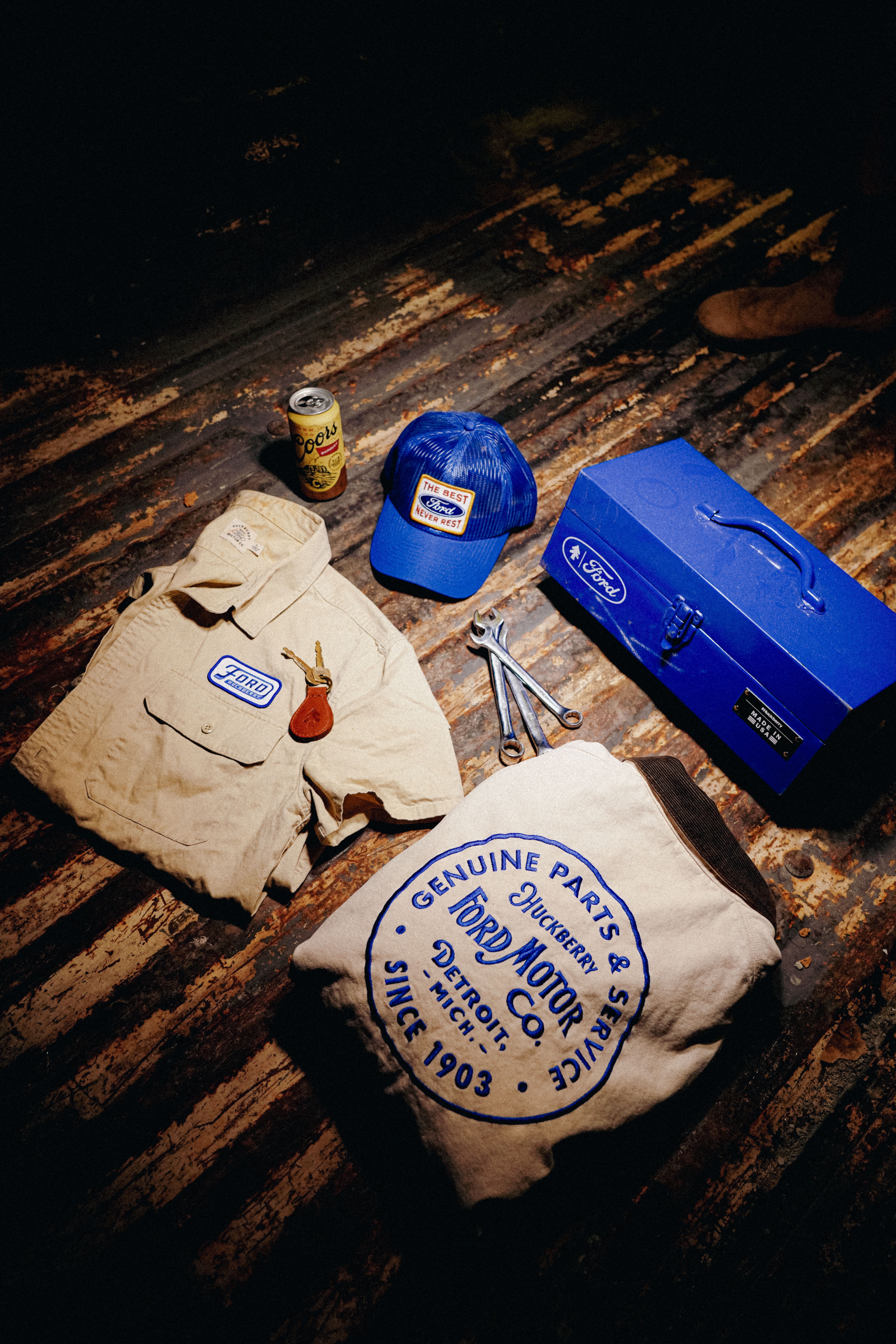 A blue hat, white shirt, white jacket, blue toolbox, and several other items spread across a wood surface