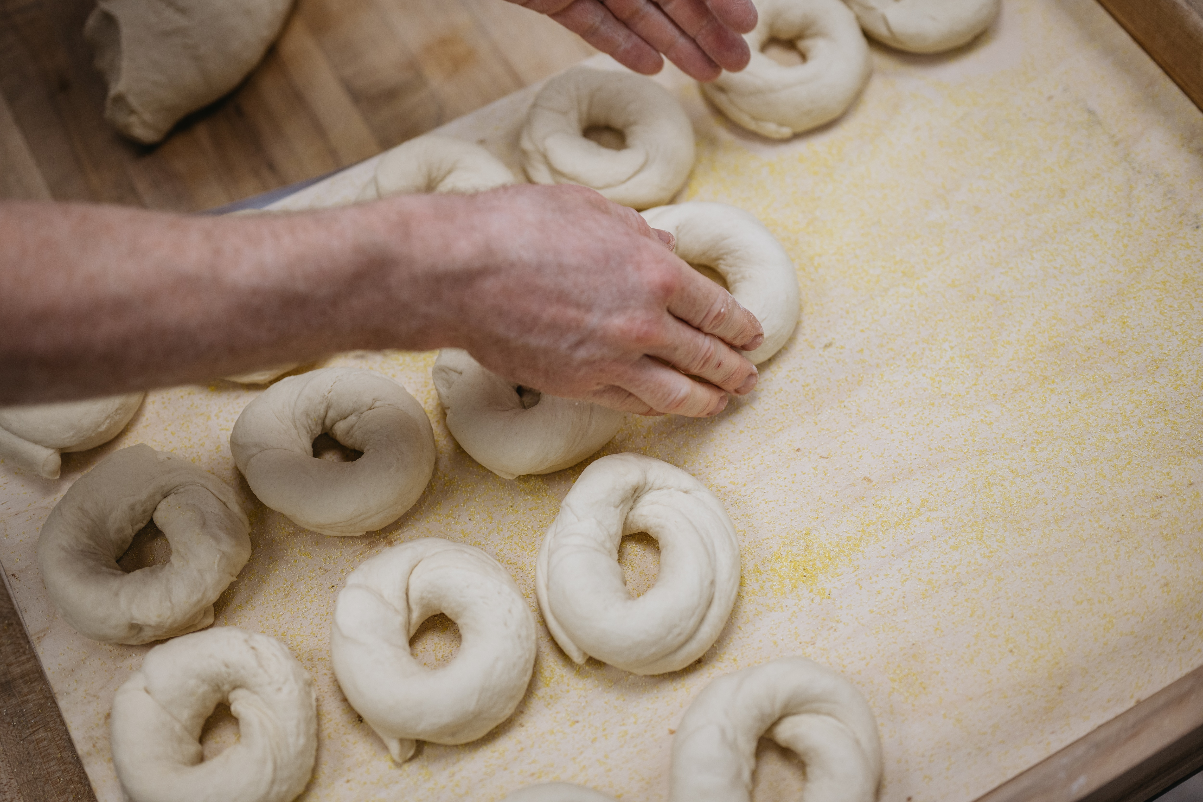 A worker at a bagel shop shapes dough into bagels.