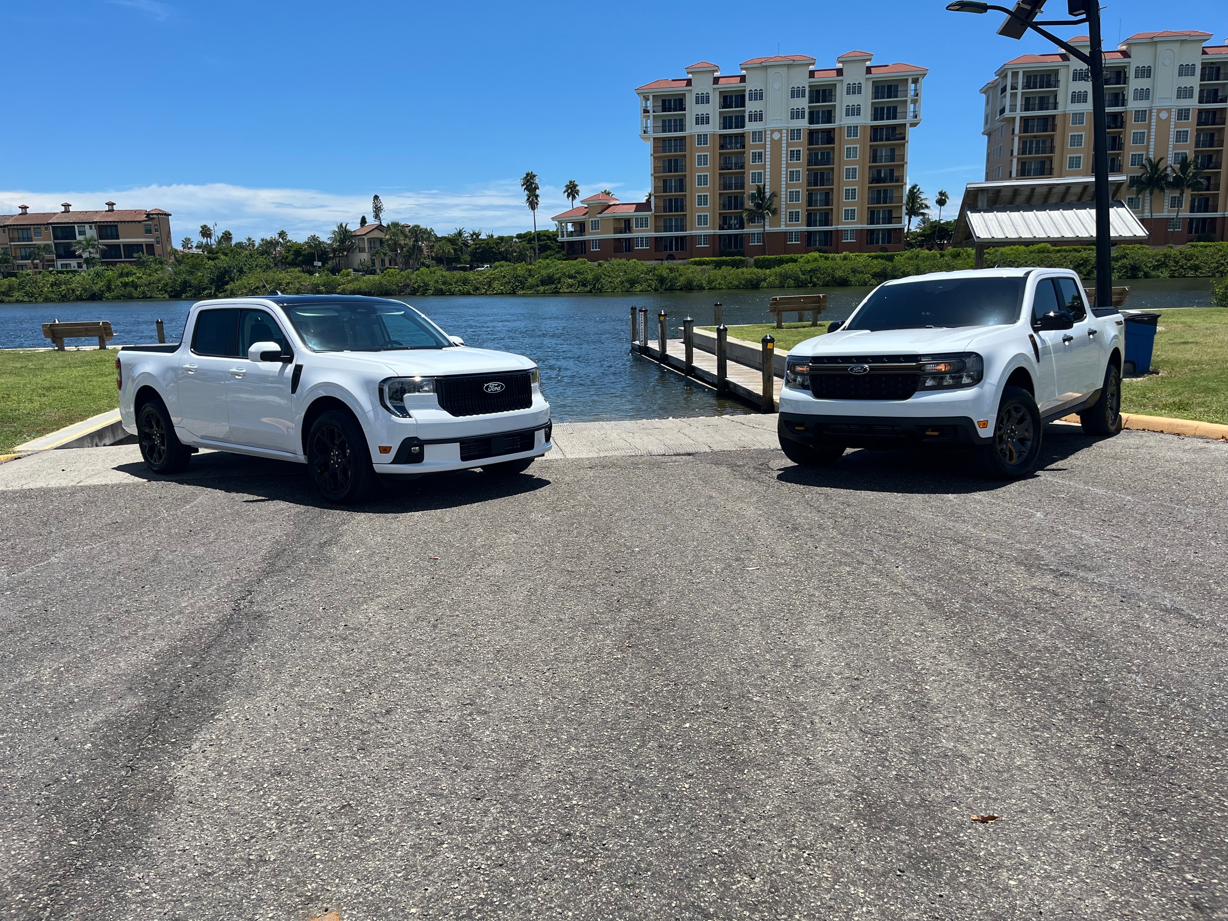 Two white Ford trucks are parked in front of a lake on a sunny day.