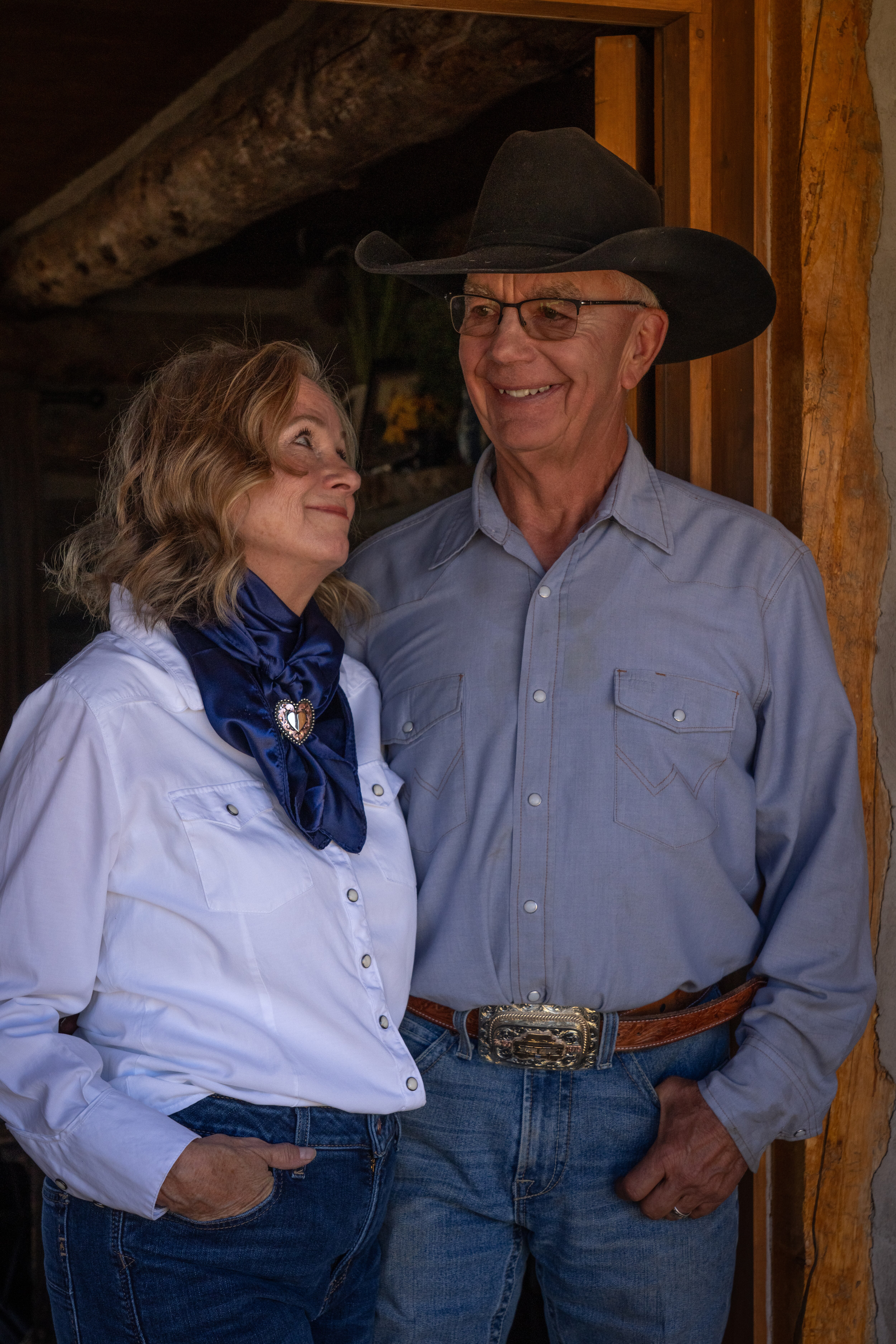 A man and woman smile at each other while posing for a photo. They are dressed in Western attire.