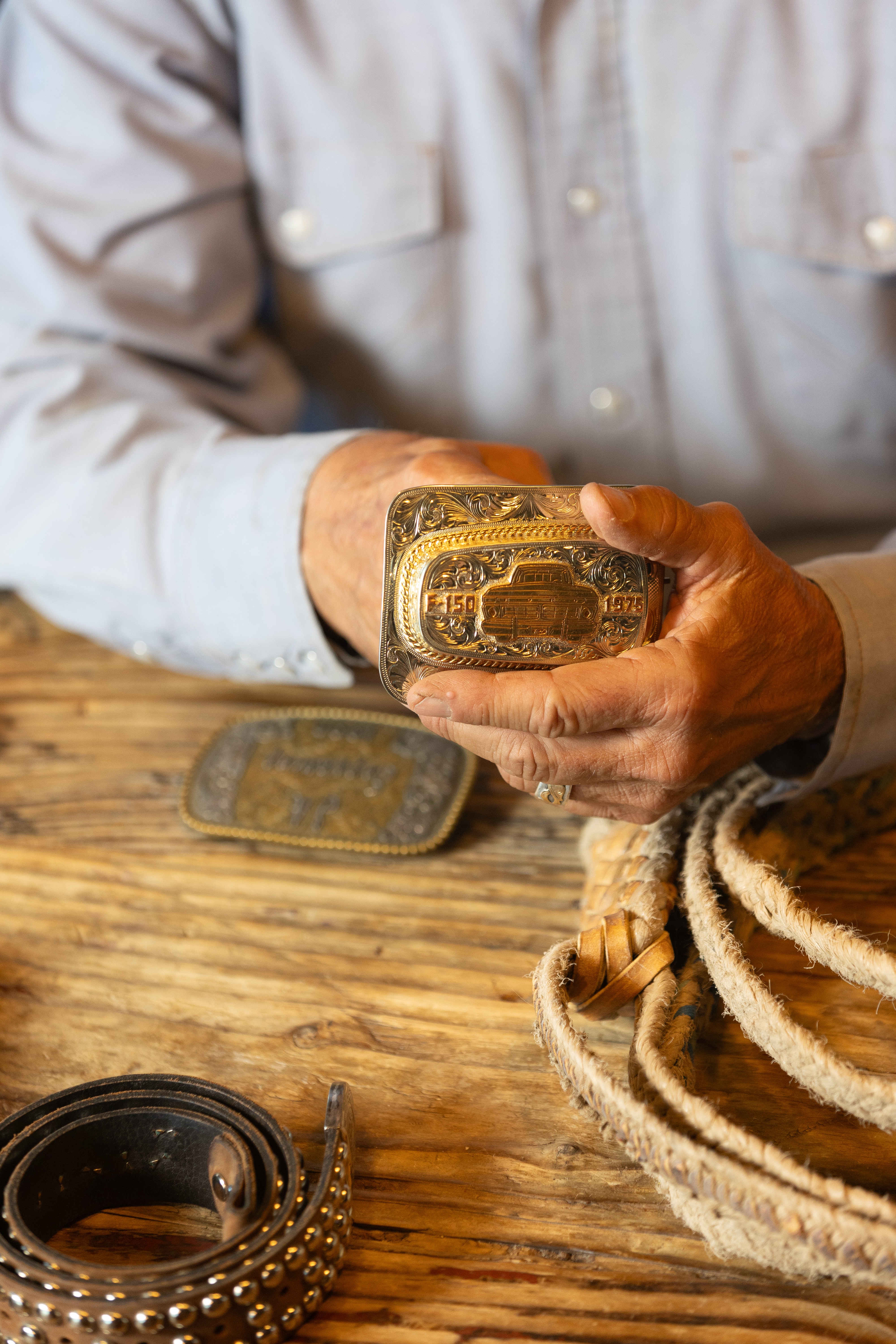A man shows the camera a gold belt buckle with a truck on it.