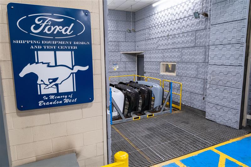 A Ford sign on the wall next to a vibrating table at a shipping and manufacturing testing plant.