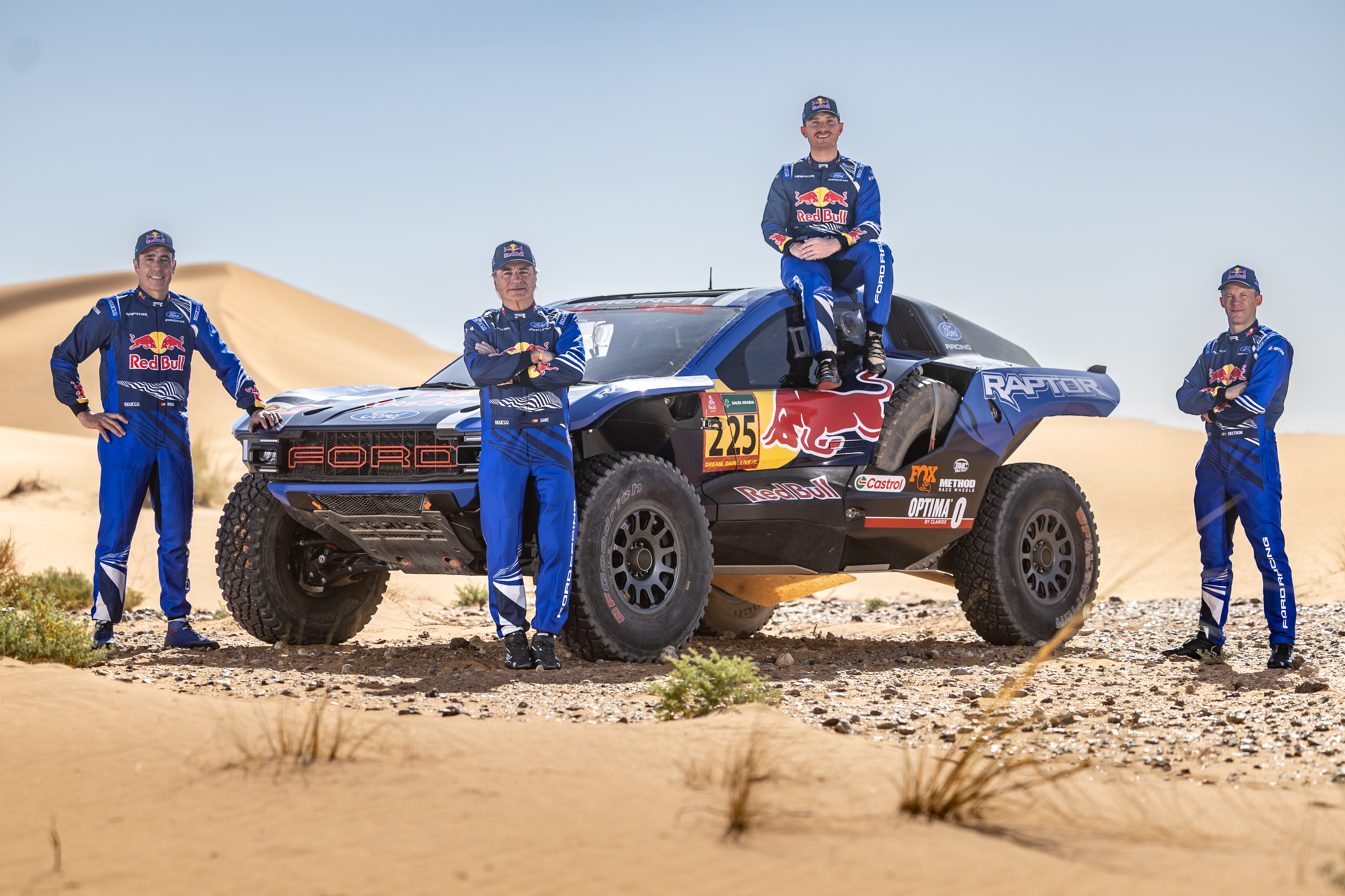 Four men in Ford Racing uniforms pose near an off-road Ford Racing vehicle in the desert.