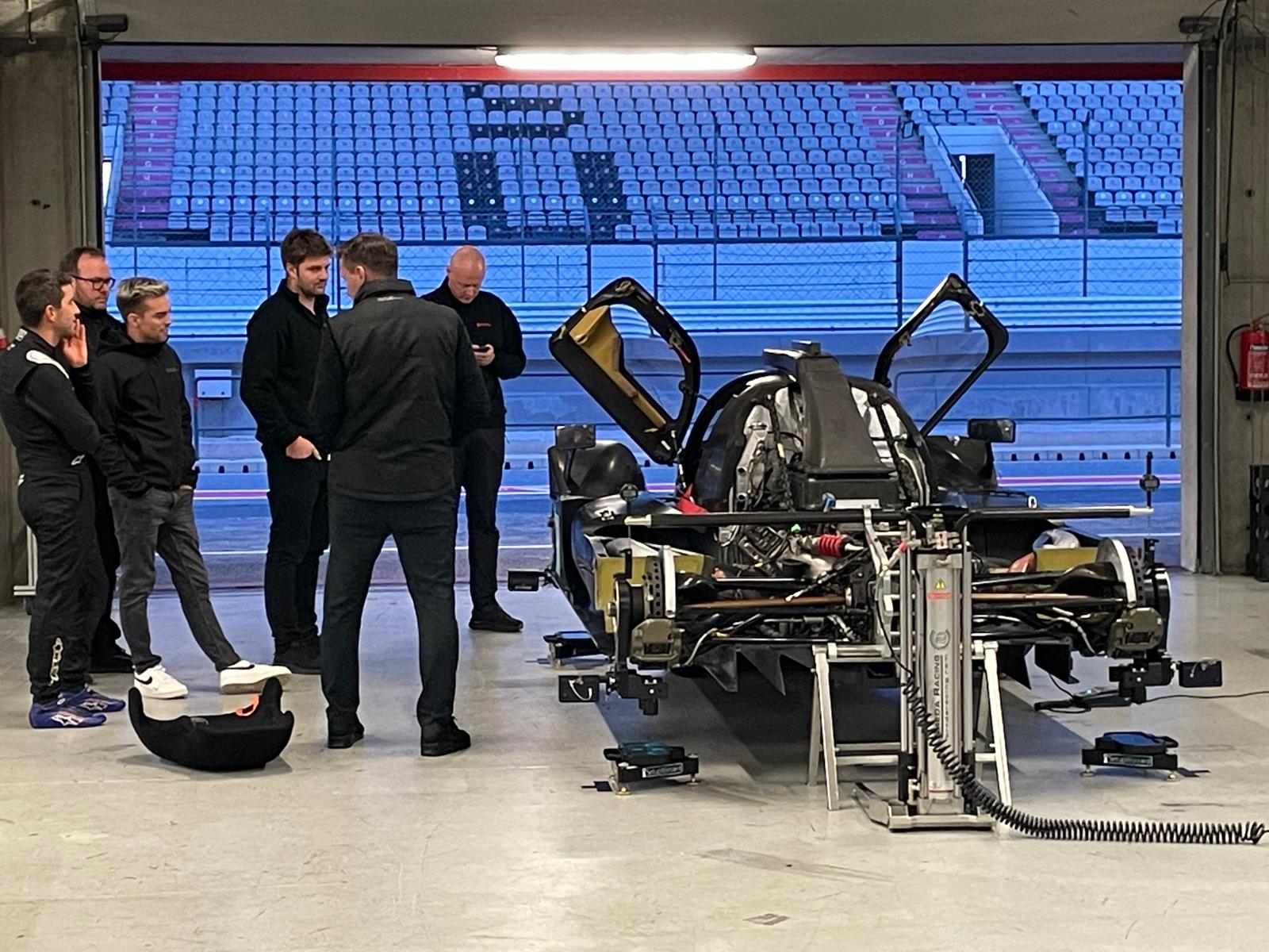 A group of people stand near a racecar being built.